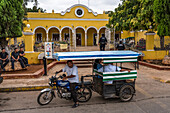 A motorcycle trailer mototaxi in front of the municipal palace or city hall of the town of Muna, Yucatan, Mexico.