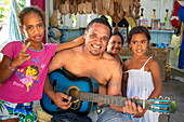Inside of a traditional house in Rangiroa, Tuamotus Islands, French Polynesia, South Pacific. Man playing guitar and singin with his family.