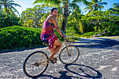 Einheimische Frau auf einem Fahrrad am Strand von Rangiroa, Tuamotu-Inseln, Französisch-Polynesien, Südpazifik.