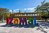 Das farbenfrohe Ortsschild von Izamal, Yucatan, Mexiko, bekannt als die Gelbe Stadt. Die historische Stadt Izamal gehört zum UNESCO-Weltkulturerbe. Dahinter befindet sich das Kloster von San Antonio.
