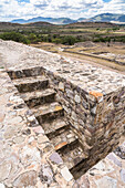 Die Treppe auf dem Dach von Gebäude A in den Ruinen der prähispanischen Zapotekenstadt Dainzu im Zentraltal von Oaxaca, Mexiko. Im Hintergrund ist der Ballspielplatz zu sehen.