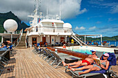 Paul Gauguin Kreuzfahrtschiff, Passagiere entspannen sich auf dem Oberdeck im Swimmingpool. Gesellschaftsinseln, Französisch-Polynesien, Südpazifik.