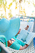 Woman with hat relaxing reading a book in a hammock, Zanzibar, Tanzania, East Africa, Africa