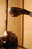 Eine Frau erhält eine Wachsbehandlung ihrer Stirn während einer ayurvedischen Behandlung