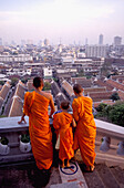 Drei Mönche stehen vor der Skyline von Bangkok