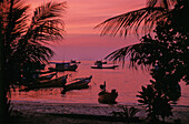 Silhouettierte Boote vor dem Strand bei Sonnenuntergang