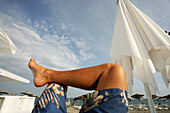 Beine eines Sonnenanbeters und Sonnenschirm am Strand