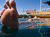 Male Swimmer Floating Alongside A Moored Boat, Low Angle View