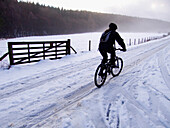 Ein einsamer Radfahrer auf einer verschneiten Landstraße