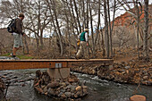 Männer, die auf einem Naturspaziergang im Red Rock State Park über einen Bach wandern.