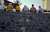 Einheimische Männer, die auf einer Steinmauer sitzen