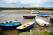 Boats In Mud Of Small Estuary By Marshes