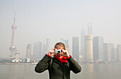 Tourist macht Foto über Bund, Huangpu Fluss mit Pudong Skyline im Hintergrund, Shanghai, China