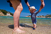 Vater hilft kleinem Jungen (6-11 Monate) beim Gehen am Strand, Soller,Mallorca,Balearen,Spanien