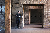 Portrait Of A Young Man Standing Against A Wall With Concrete And Brick Facade; Rome, Italy
