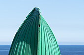 Nahaufnahme der Unterseite des Bugs eines grün gestrichenen Holzboots und des ruhigen Wassers und blauen Himmels im Hintergrund; South Shields, Tyne And Wear, England.