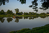 Eine ruhige Szene mit Bäumen, die sich im Flusswasser spiegeln und einem blauen Himmel; Chiang Rai, Thailand