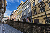 Colourful Residential Buildings And A Wall Along A Narrow Cobblestone Road; Prague, Czechia