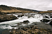 Water Flowing Over Rocks On A Landscape Under A Cloudy Sky; Iceland