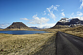An Asphalt Road Along The Coast With Snow-Capped Mountains, Snaefellsnes Peninsula; Iceland