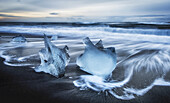 Jagged pieces of broken ice laying on the sandy shore at the edge of the ocean water; Iceland