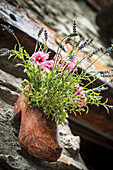 Ein mit Holzschuhen geschnitzter Blumentopf entlang der alten Kopfsteinpflasterstraßen von Dolonne, in der Nähe von Courmayeur; Aosta-Tal, Italien