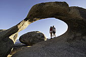 Junge Kinder stehen unter einem natürlichen Felsbogen, Alabama Hills; Kalifornien, Vereinigte Staaten von Amerika