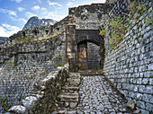 Stone walls and path of the Kotor Fortress with mountain peak and blue sky; Kotor, Montenegro