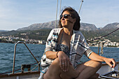 Eine Frau sitzt auf dem Deck eines Segelbootes mit windzerzausten Haaren und schaut in die Kamera an der Küste von Montenegro; Montenegro