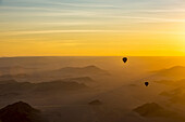 Silhouette von Heißluftballons im goldenen Himmel über den Sanddünen bei Sonnenaufgang in der Namib-Wüste; Sossusvlei, Hardap-Region, Namibia.