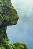 Form eines Kopfes in natürlichen, mit grünem Moos bewachsenen Felsen neben dem Skogafoss-Wasserfall; Island