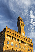 Alte Steinburg und Turm mit dramatischen Wolken und blauem Himmel, der bei Sonnenuntergang orange leuchtet; Florenz, Toskana, Italien.
