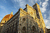 Large decorative cathedral with tower and dome with blue sky and clouds glowing orange at sunset