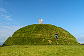 Man walking up Thufa grassy dome with fish drying house on top (art installation by Olof Nordal); Reykjavik, Iceland