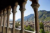 Palace stone columns frames an alpine village in the background with mountains and blue sky; Trento, Trento, Italy