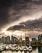 Condominium buildings and sailboats moored in the harbour under dark clouds; Vancouver, British Columbia, Canada