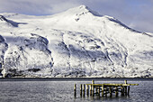 Der alte Hafen und die schneebedeckten Berge rund um Djupavik; Djuupavik, Westfjorde, Island
