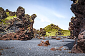 Colourful lava rock formations scattered across the black sand beach in Snaefellsjokull National Park; Iceland
