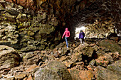 Two female tourists hiking through the lava tube caves; Iceland