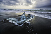 Piece of ice sitting on the shore of Iceland with dramatic stormy skies in behind it; Iceland