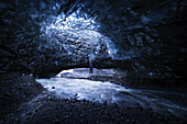 Mann steht unter einer Öffnung in der Eishöhle, während er unter einem Gletscher spazieren geht: Island