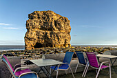 Colourful restaurant patio along the Atlantic coast with a large sea stack along the shore; South Shields, Tyne and Wear, England