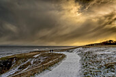 Zwei Gestalten, die in der Abenddämmerung auf einem verschneiten Weg entlang der Küste spazieren; South Shields, Tyne and Wear, England.