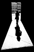 Silhouette und Schatten einer Frau, die durch einen Durchgang auf einem Stadtplatz in Richtung Rathaus geht; Arles, Provence Alpes Cote D'Azur, Frankreich.