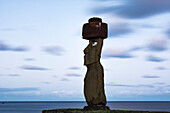 Ein einzelner Moai vor einem blauen Hintergrund aus Himmel, Wolken und Meer; Osterinsel, Chile.