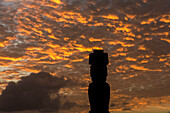 A single moai is silhouetted againt the bright red sunset sky; Easter Island, Chile
