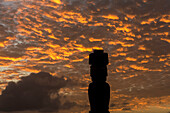 Ein einzelner Moai hebt sich gegen den leuchtend roten Himmel bei Sonnenuntergang ab; Osterinsel, Chile.