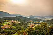 Sonnenlicht leuchtet durch den bedeckten Himmel über den sanften Hügeln von Lugano; Lugano, Tessin, Schweiz