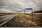 Straßen- und Tundra-Landschaft mit Flughafenschild am Straßenrand; Island