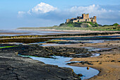 Bamburgh Castle with the tide out showing rocky coastline; Bamburgh, Northumberland, England